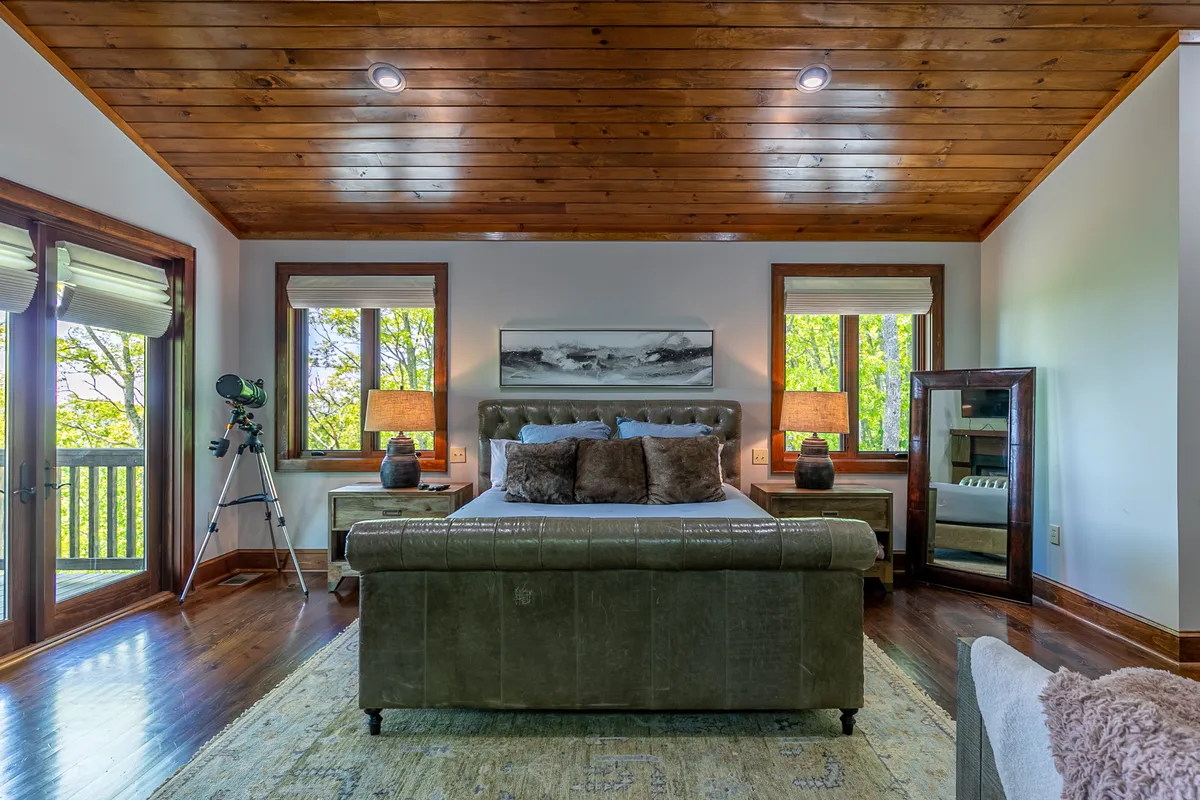 A serene king bedroom with a large upholstered bed, window views, decorative lamps, and a telescope positioned for stargazing. The tranquil mood and thoughtful details create a welcoming retreat for relaxation.