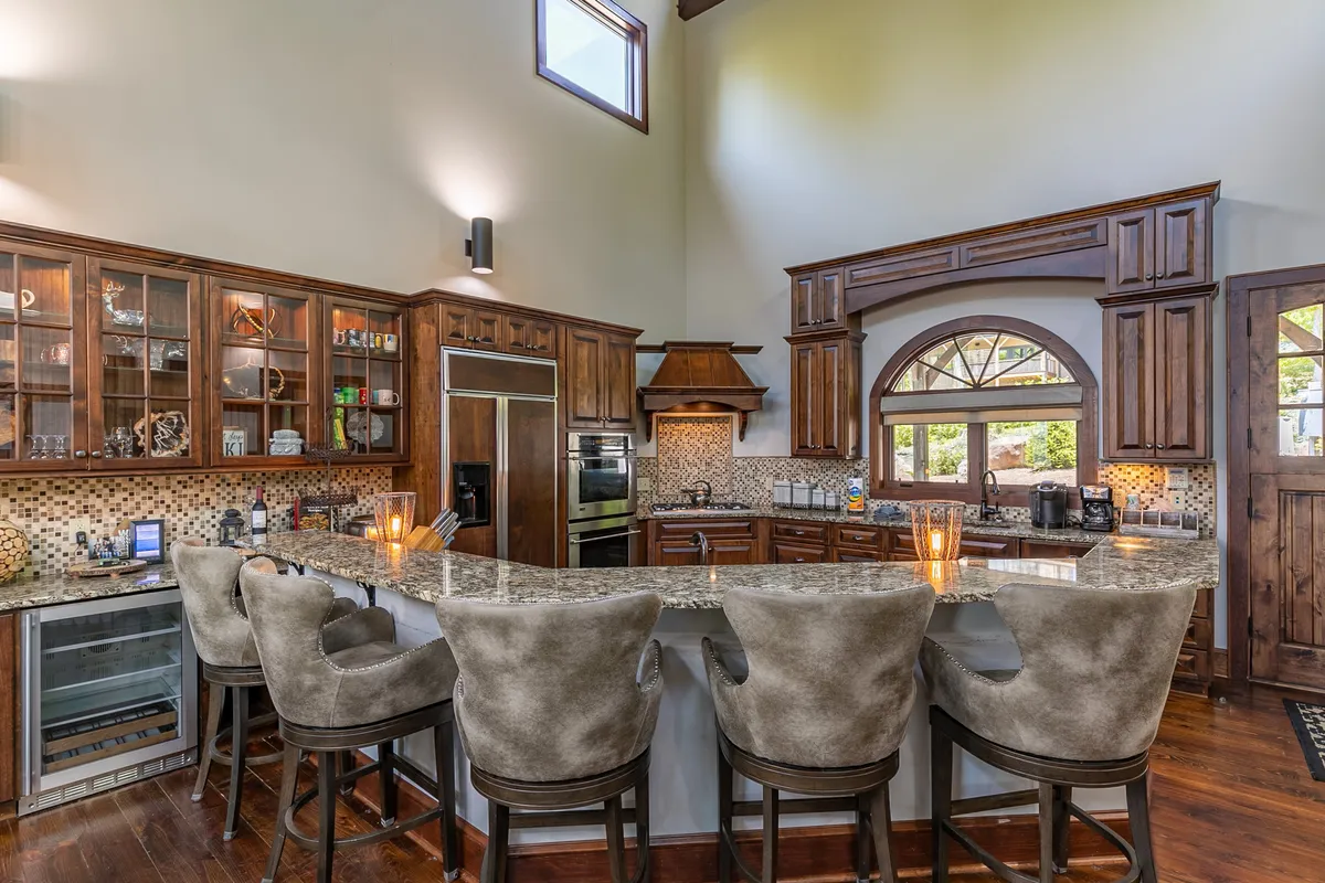 A welcoming kitchen with a large granite island at the center, surrounded by warm wood cabinetry and bar stools. There is a window offering a view, and the layout encourages both culinary creativity and casual conversation. The granite countertop, bar seating, and ample workspace are all on display, ideal for group meal preparation or entertaining guests.