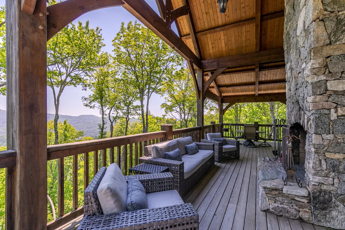 An expansive covered porch furnished with comfortable seating and centered around a striking stone fireplace. The porch opens to panoramic mountain views, inviting guests to enjoy the outdoor fire and layered vistas in every season.