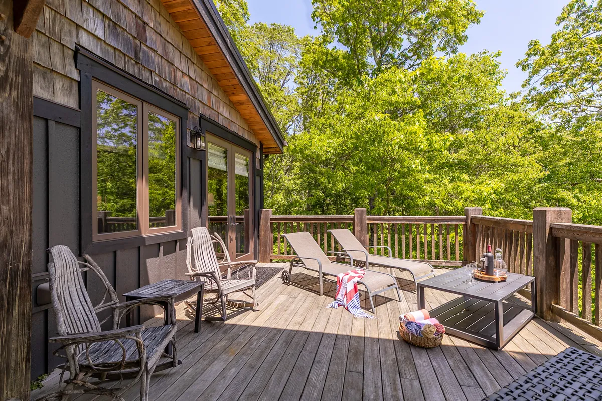 This image showcases an inviting exterior deck area, complete with lounge chairs, a coffee table, and a sturdy deck railing set amidst lush surrounding trees. The atmosphere is calm, perfect for enjoying the outdoors in comfort and privacy.