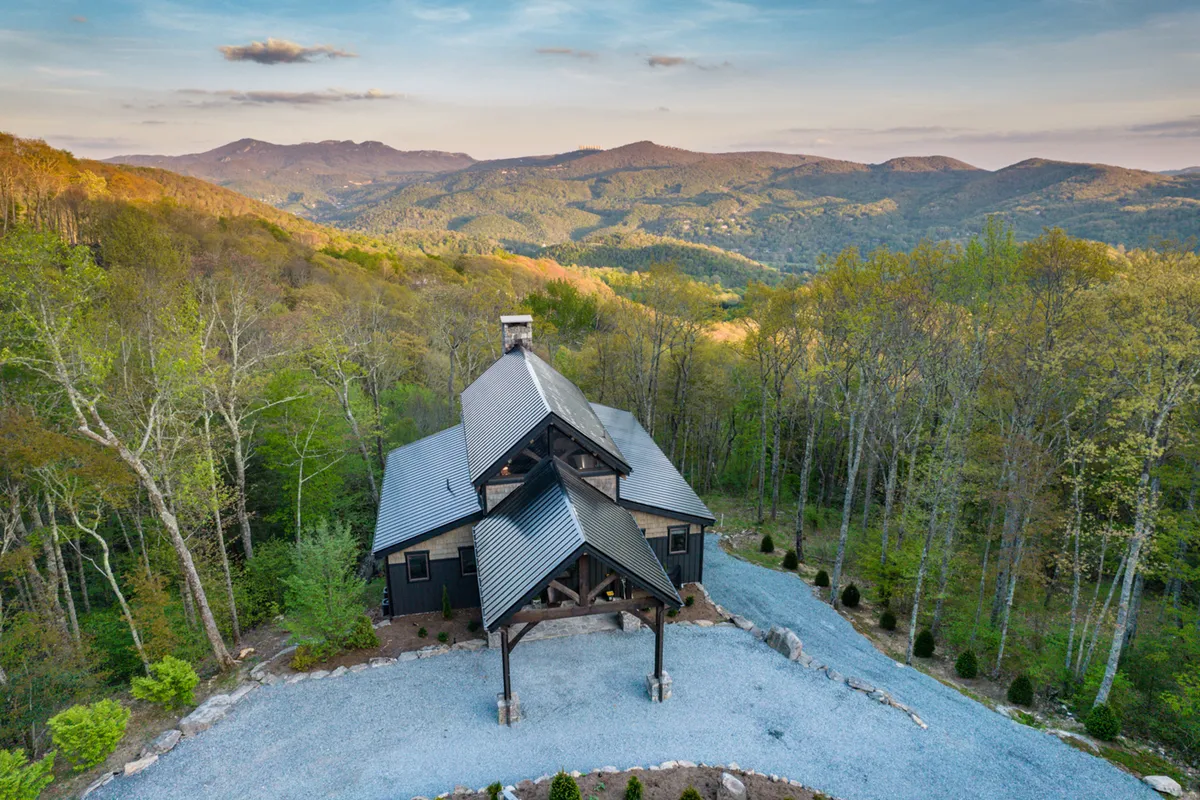 The exterior of the property set against a backdrop of mountains and trees, with a welcoming driveway and ample space for outdoor activities. The home’s location underscores its retreat-like feel and potential for group adventure.