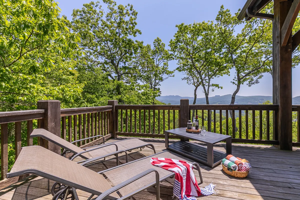 This image captures a tranquil deck setting with lounge chairs, a coffee table, and a basket of blankets, all oriented to maximize the stunning mountain views. The scene conveys a sense of peaceful relaxation and direct access to nature from the property.