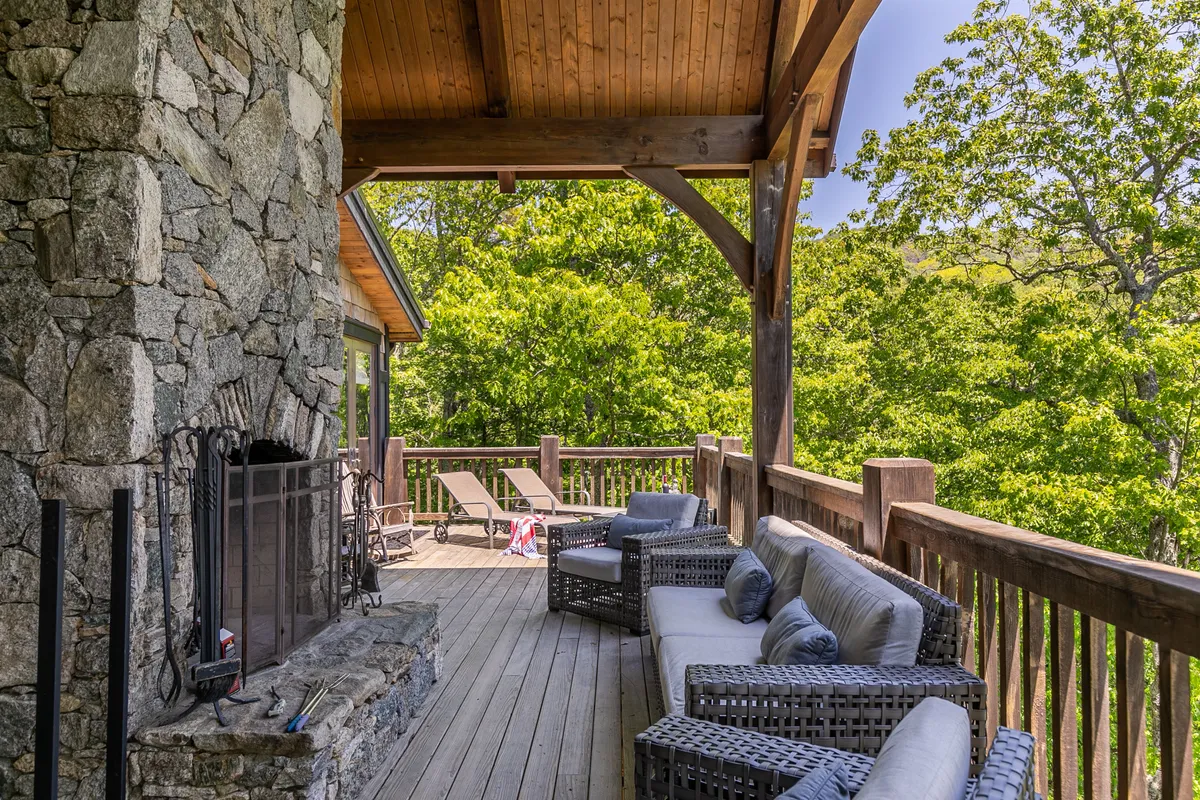 A spacious outdoor deck is appointed with a stone fireplace, comfortable seating, and lush greenery. The mountain view is visible, and the scene feels inviting for family picnics, impromptu games, and gatherings, reminiscent of the Great Lawn and communal spaces described.