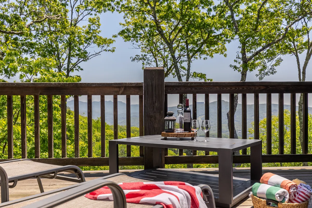 An inviting outdoor table set with a bottle of wine and glasses, surrounded by lush greenery and distant mountain views. The relaxed setting hints at an afternoon or evening spent socializing, relaxing, or enjoying a wine tasting with friends amidst nature.