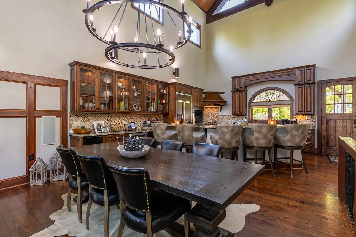 An expansive interior view where the kitchen island with bar seating flows into a large dining table. Warm wood cabinetry and chandelier lighting add a touch of luxury, while the open layout encourages group cooking sessions and shared meals.