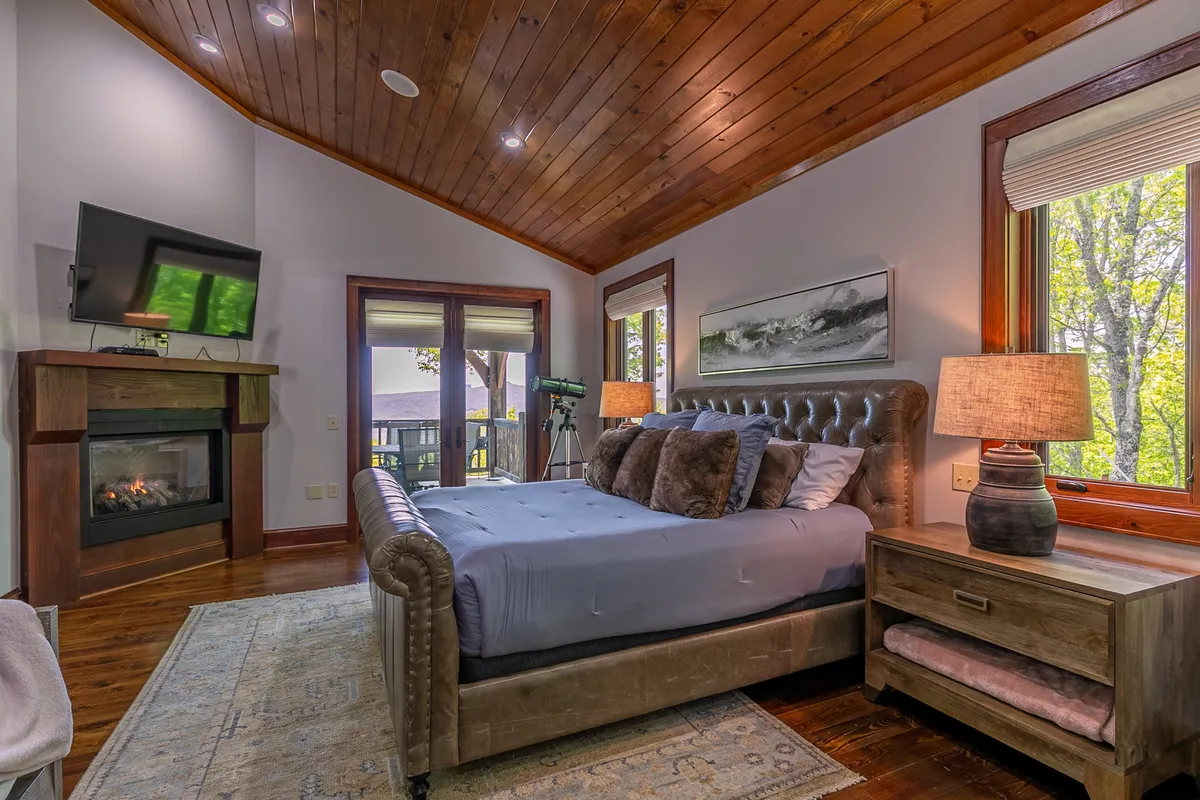 A tranquil king bedroom featuring a king-sized bed dressed in premium linens, a cozy fireplace, and large windows offering views and natural light. Decorative lamps and a telescope add a touch of luxury and relaxation, while the intimate atmosphere invites restful retreat.