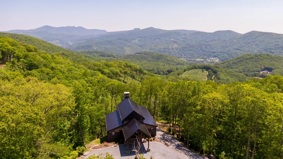 A modern house is nestled in a lush forest with expansive mountain views stretching into the distance. The scene captures the tranquility and adventure of the outdoors, inviting guests to explore hiking trails, enjoy nature walks, or stargaze in the evenings.