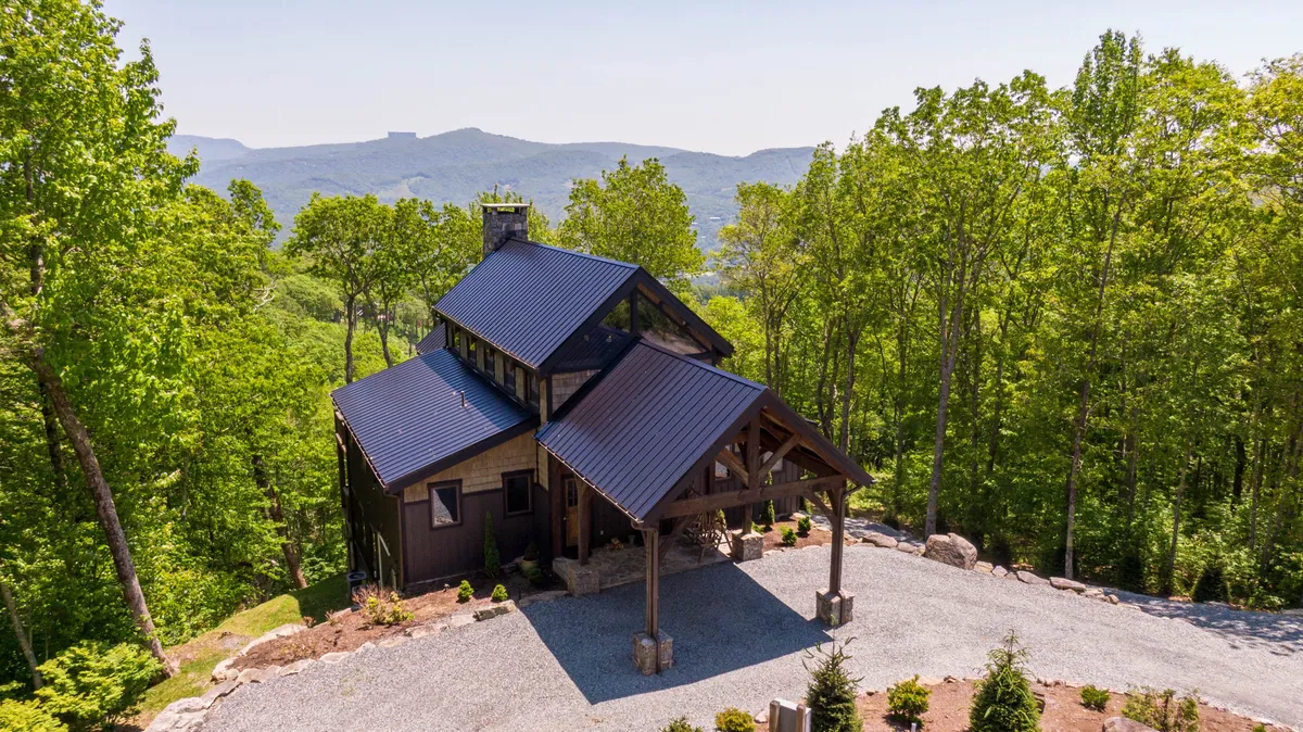 The hero image showcases a modern timber-framed cabin nestled among lush trees, set against a backdrop of sweeping Blue Ridge Mountain vistas. The spacious deck invites guests to enjoy sunrises, stargazing, and tranquil outdoor gatherings, while the architectural details exude luxury and warmth.