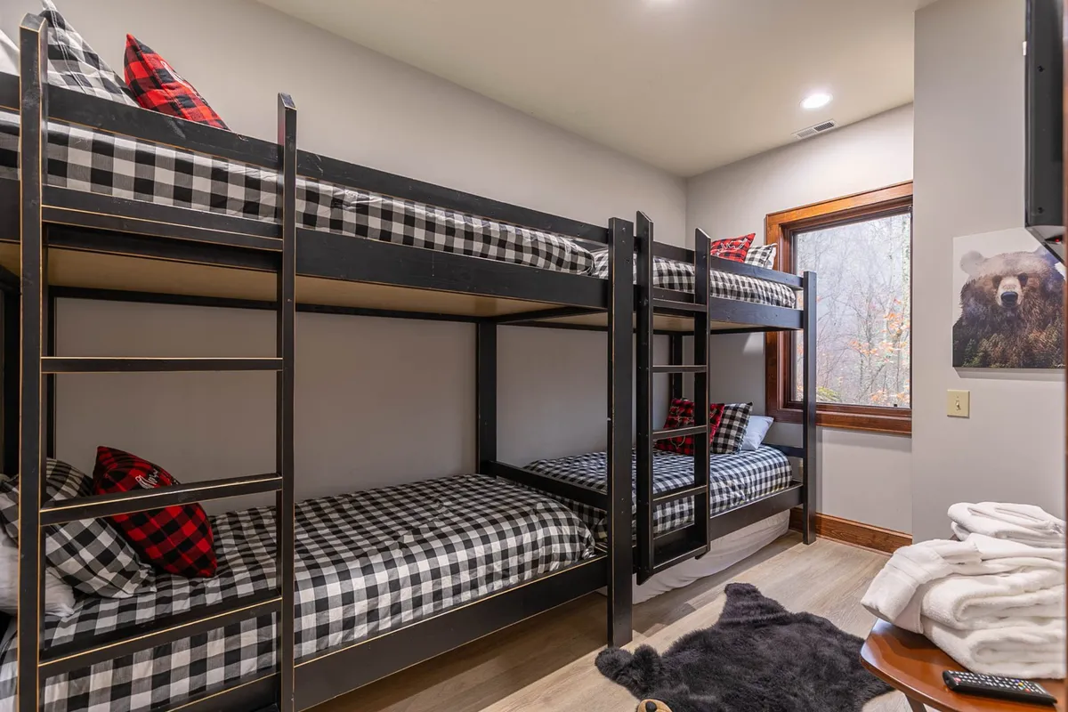 A playful and inviting bunkroom with multiple twin bunk beds, decorative pillows, and a window offering natural light. The space radiates a sense of fun and comfort, making it an ideal haven for children or multi-generational groups.